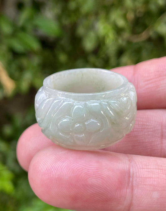 Close-up of intricately hand-carved floral petals and organic curves on an icy apple green Burmese jade ring
