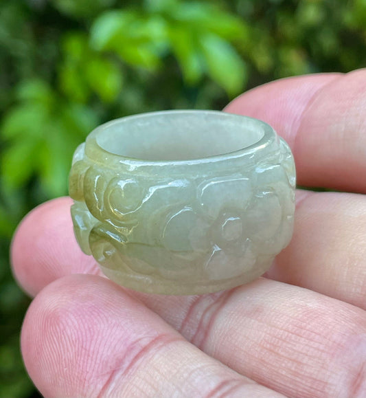 Close-up of continuous hand-carved floral and swirl design on an icy apple green and spinach green Burmese jade ring