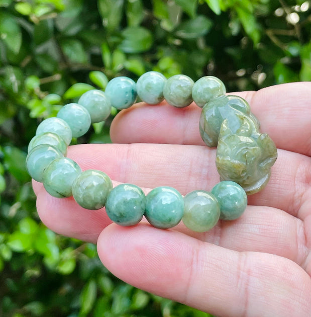 10mm certified Type A Burmese jade beads showing semi-translucent luster, mossy green hues, and a hand-carved Pixiu pendant on the wrist