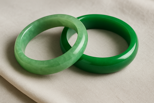 Two jade bangles on a soft off-white fabric—one with subtle, natural color variations and translucency, the other a richer, more opaque green—highlighting the visual difference between natural and treated jade.