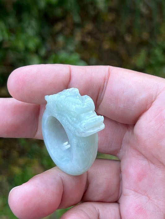Close-up of defined dragon head and fine textural detailing on a semi-translucent icy bluish-white Burmese jade ring