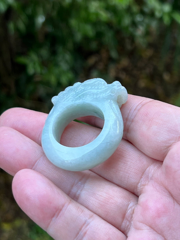 Close-up of defined dragon head and fine textural detailing on a semi-translucent icy bluish-white Burmese jade ring