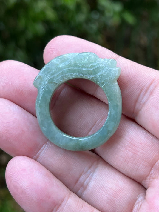 Close-up of layered carving and well-defined dragon body on a semi-translucent icy green Burmese jade ring