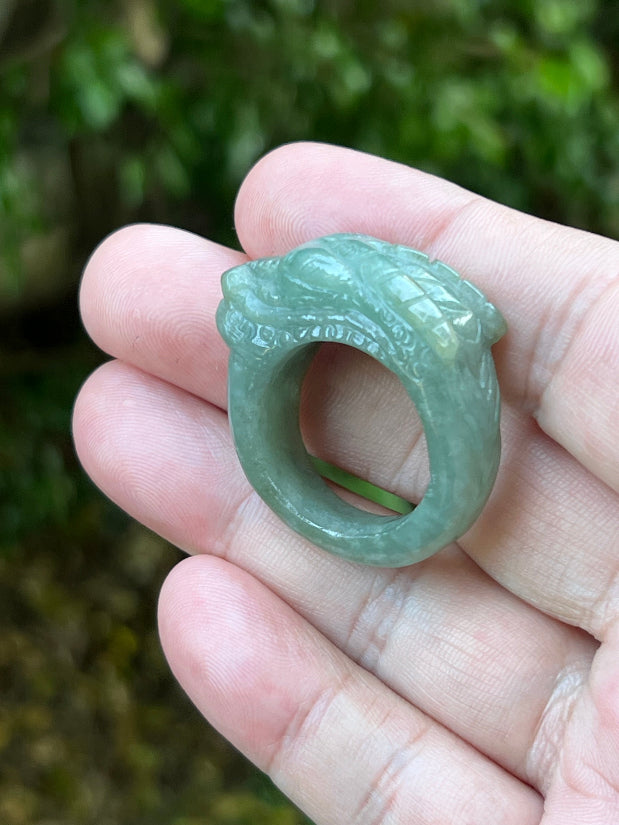 Close-up of pronounced facial definition and raised dragon carving on a semi-translucent icy green Burmese jade ring