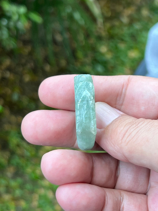 Close-up of precise hand-carved dragon detailing and textured scales on a semi-translucent icy green Burmese jade ring