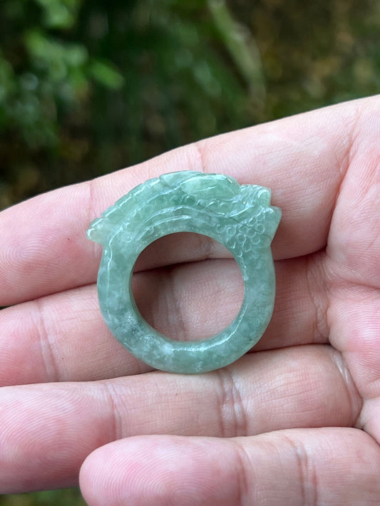 Close-up of precise hand-carved dragon detailing and textured scales on a semi-translucent icy green Burmese jade ring