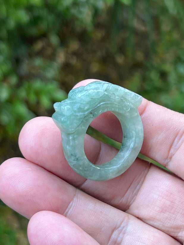 Close-up of precise hand-carved dragon detailing and textured scales on a semi-translucent icy green Burmese jade ring