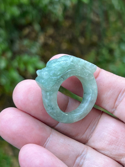 Close-up of precise hand-carved dragon detailing and textured scales on a semi-translucent icy green Burmese jade ring