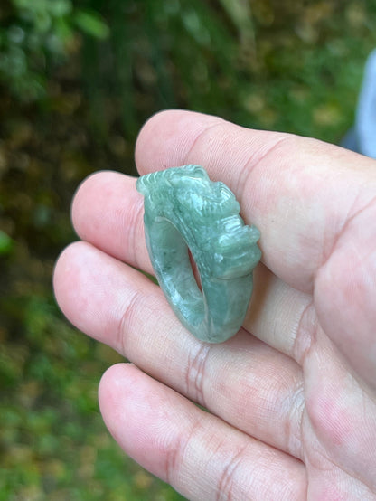 Close-up of precise hand-carved dragon detailing and textured scales on a semi-translucent icy green Burmese jade ring