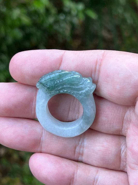 Close-up of layered scale work and detailed hand-carved dragon on a semi-translucent icy white and green Burmese jade ring