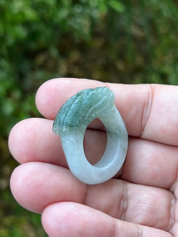 Close-up of layered scale work and detailed hand-carved dragon on a semi-translucent icy white and green Burmese jade ring