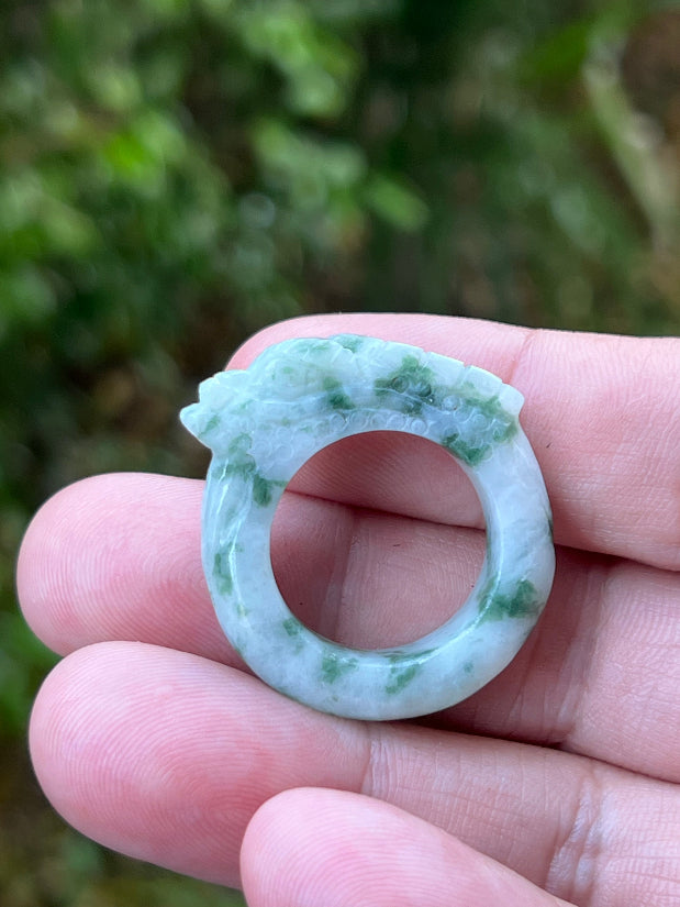 Close-up of smooth hand-carved dragon detailing and moss-in-snow green patches on white Burmese jade ring