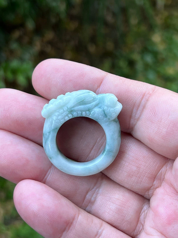 Close-up of rounded fluid carving and bead-like detailing on an icy white and moss green Burmese jade ring