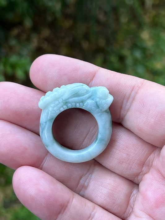 Close-up of rounded fluid carving and bead-like detailing on an icy white and moss green Burmese jade ring