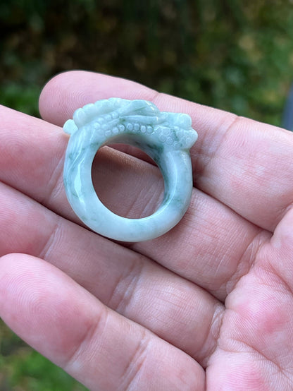 Close-up of rounded fluid carving and bead-like detailing on an icy white and moss green Burmese jade ring