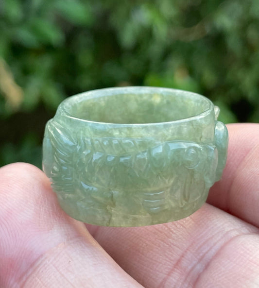 Close-up of repeating hand-carved fish motif and graceful flow on an icy translucent emerald green Burmese jade ring