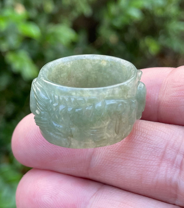 Close-up of repeating hand-carved fish motif and graceful flow on an icy translucent emerald green Burmese jade ring