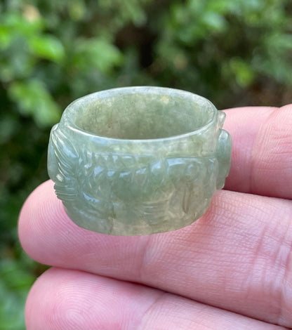 Close-up of repeating hand-carved fish motif and graceful flow on an icy translucent emerald green Burmese jade ring