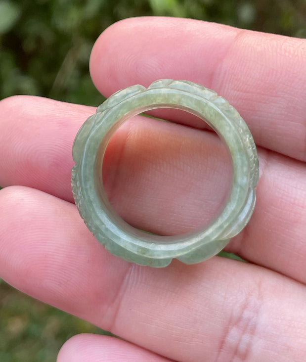 Close-up of repeating hand-carved fish motif and graceful flow on an icy translucent emerald green Burmese jade ring