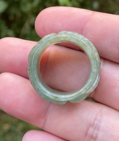 Close-up of repeating hand-carved fish motif and graceful flow on an icy translucent emerald green Burmese jade ring