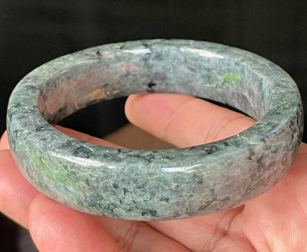 Close-up of fine crystalline texture and rich moss green swirls on icy black and grey jadeite bangle
