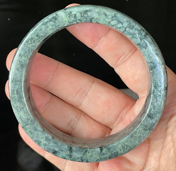 Close-up of fine crystalline texture and rich moss green swirls on icy black and grey jadeite bangle