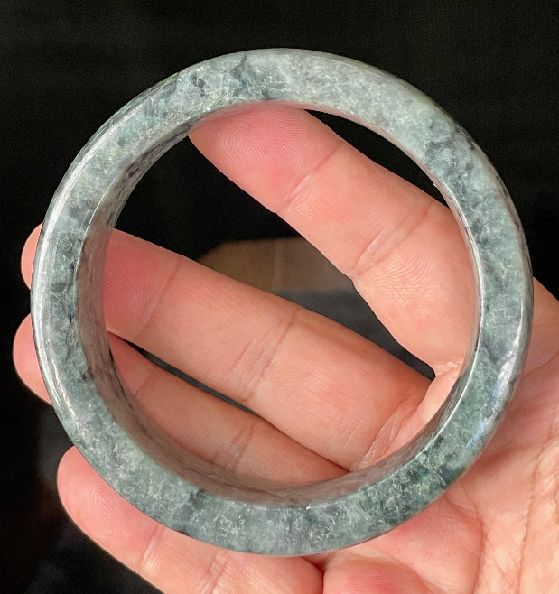 Close-up of fine crystalline texture and rich moss green swirls on icy black and grey jadeite bangle