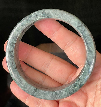 Close-up of fine crystalline texture and rich moss green swirls on icy black and grey jadeite bangle