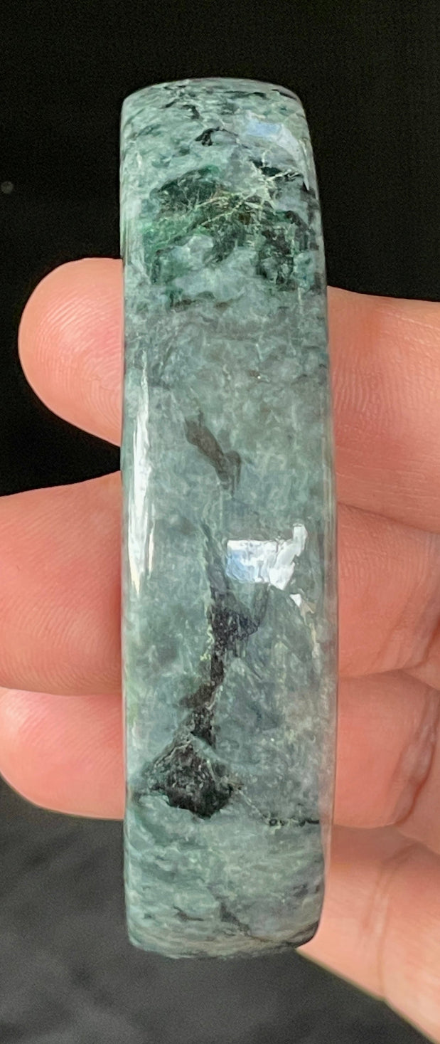 Close-up of fine crystalline texture and rich moss green swirls on icy black and grey jadeite bangle