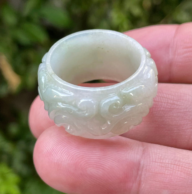 Close-up of intricately hand-carved floral petals and organic curves on an icy apple green Burmese jade ring