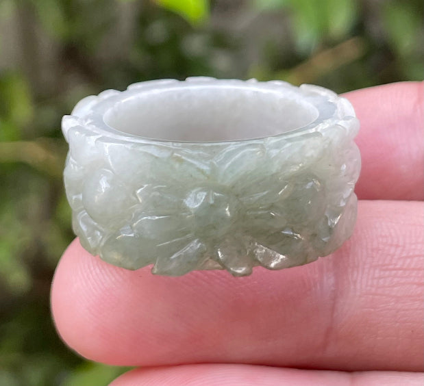Close-up of intricate hand-carved floral petals and organic curves on an icy apple green Burmese jade ring