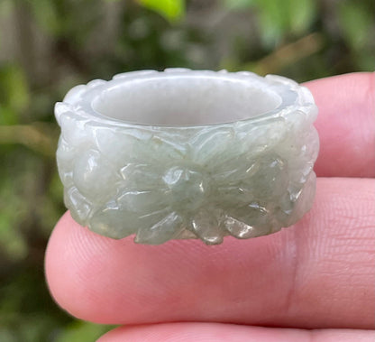 Close-up of intricate hand-carved floral petals and organic curves on an icy apple green Burmese jade ring