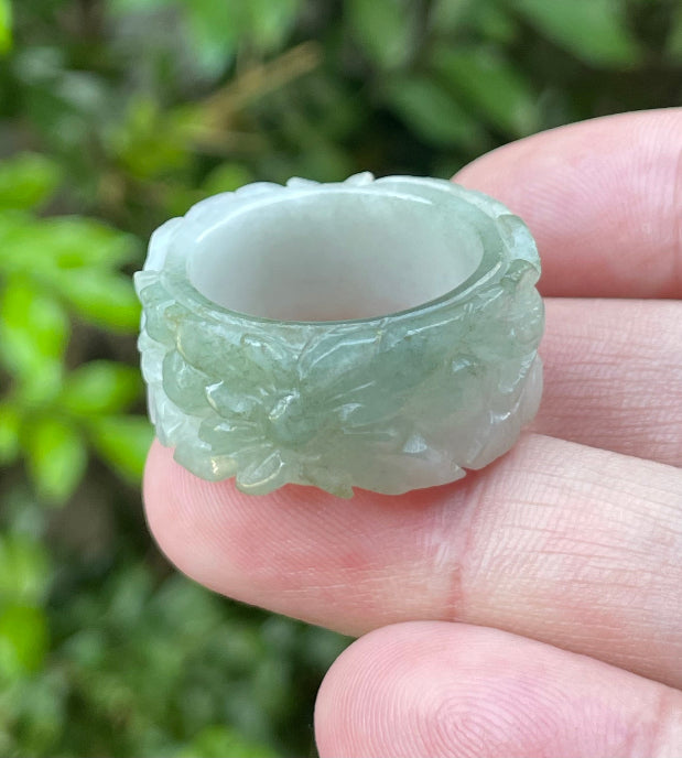 Close-up of intricate hand-carved floral petals and organic curves on an icy apple green Burmese jade ring