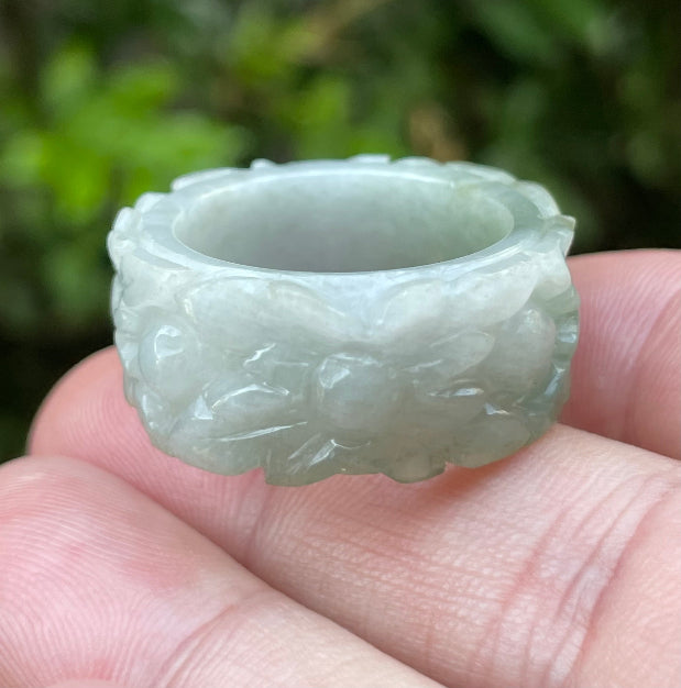 Close-up of intricate hand-carved floral petals and organic curves on an icy apple green Burmese jade ring