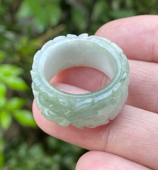 Close-up of intricate hand-carved floral petals and organic curves on an icy apple green Burmese jade ring