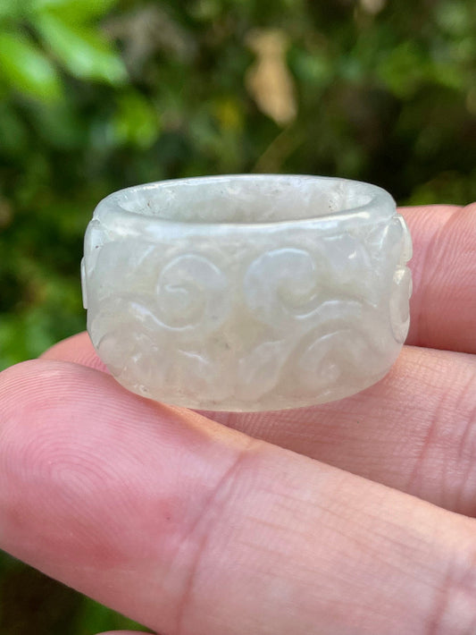 Close-up of swirling clouds and delicate floral elements on an icy translucent light apple green Burmese jade ring