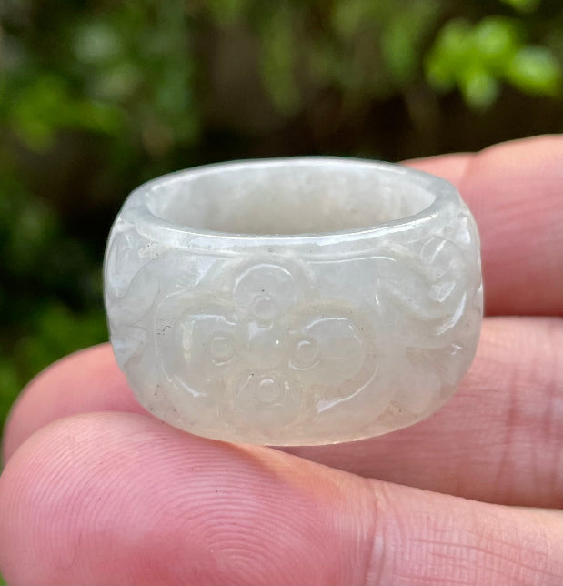 Close-up of swirling clouds and delicate floral elements on an icy translucent light apple green Burmese jade ring
