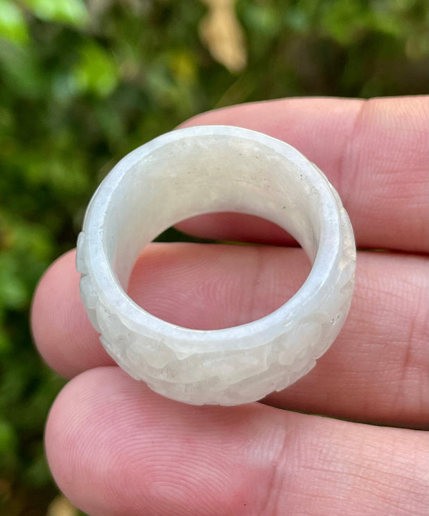 Close-up of swirling clouds and delicate floral elements on an icy translucent light apple green Burmese jade ring