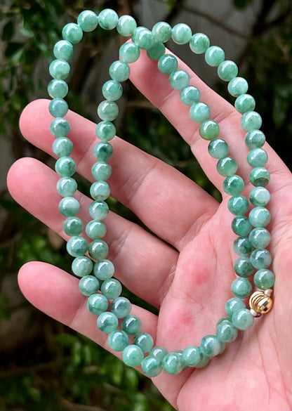 Woman wearing a 23-inch elegant natural Grade A jade bead necklace with a gold-tone twist clasp