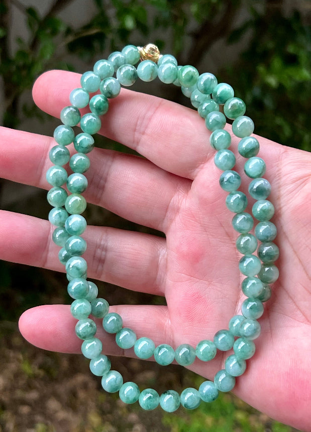 Woman wearing a 23-inch elegant natural Grade A jade bead necklace with a gold-tone twist clasp