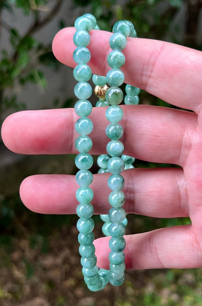 Woman wearing a 23-inch elegant natural Grade A jade bead necklace with a gold-tone twist clasp