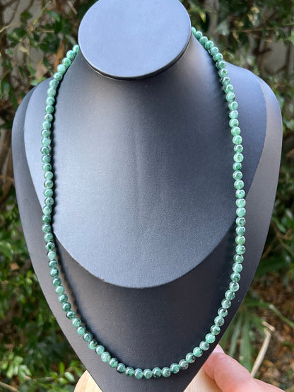 Woman wearing a 22-inch elegant natural Grade A jade bead necklace with a red-tone twist clasp