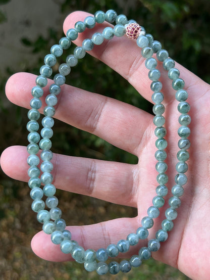 Woman wearing a 22-inch elegant natural Grade A jade bead necklace with a red-tone twist clasp