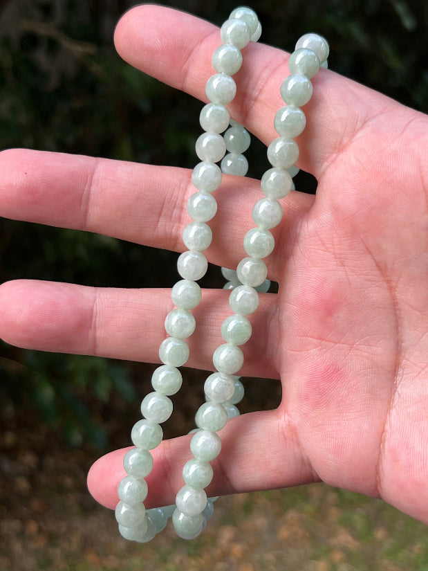 Woman wearing a 22-inch elegant natural Grade A jade bead necklace with a red-tone twist clasp