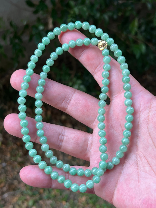 Woman wearing a 23-inch elegant natural Grade A jade bead necklace with a gold-tone twist clasp