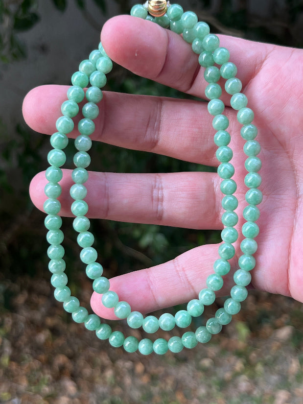 Woman wearing a 23-inch elegant natural Grade A jade bead necklace with a gold-tone twist clasp