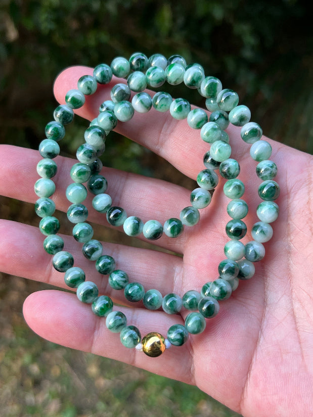 Woman wearing a 22-inch elegant natural Grade A jade bead necklace with a gold-tone twist clasp