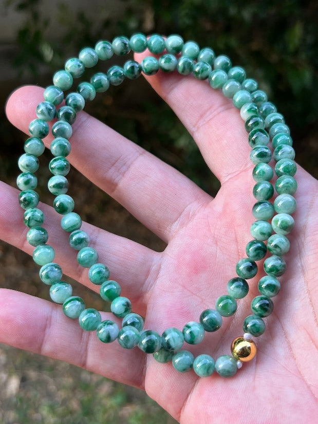 Woman wearing a 22-inch elegant natural Grade A jade bead necklace with a gold-tone twist clasp