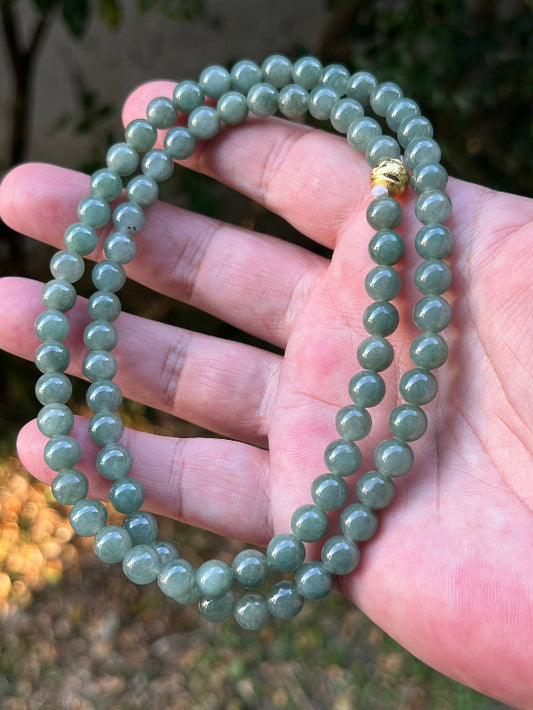 Woman wearing a 23-inch elegant natural Grade A jade bead necklace with a gold-tone twist clasp