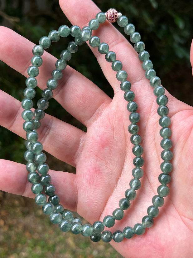 Woman wearing a 23-inch elegant natural Grade A jade bead necklace with a red-tone twist clasp